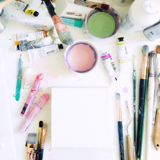 looking-down-at-an-artists-messy-white-desktop-with-art-supplies-and-a-blank-canvas_t20_AemJdW